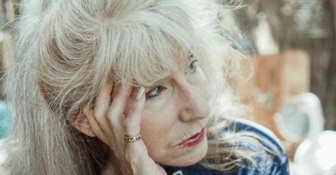 An introspective senior woman in thought, sitting outdoors on a sunny day.